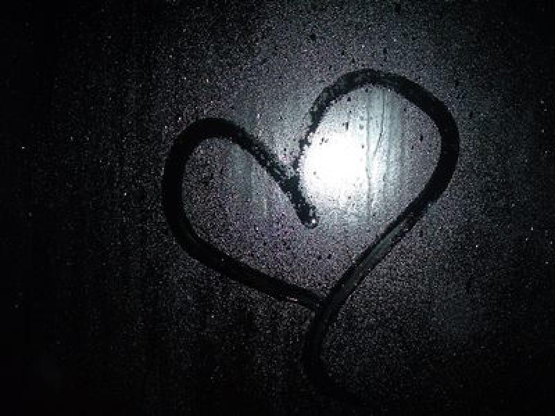 A heart is drawn into a foggy window. The moon is in the center of the heart and is illuminating the water droplets on the window which shows the heart through contrast.