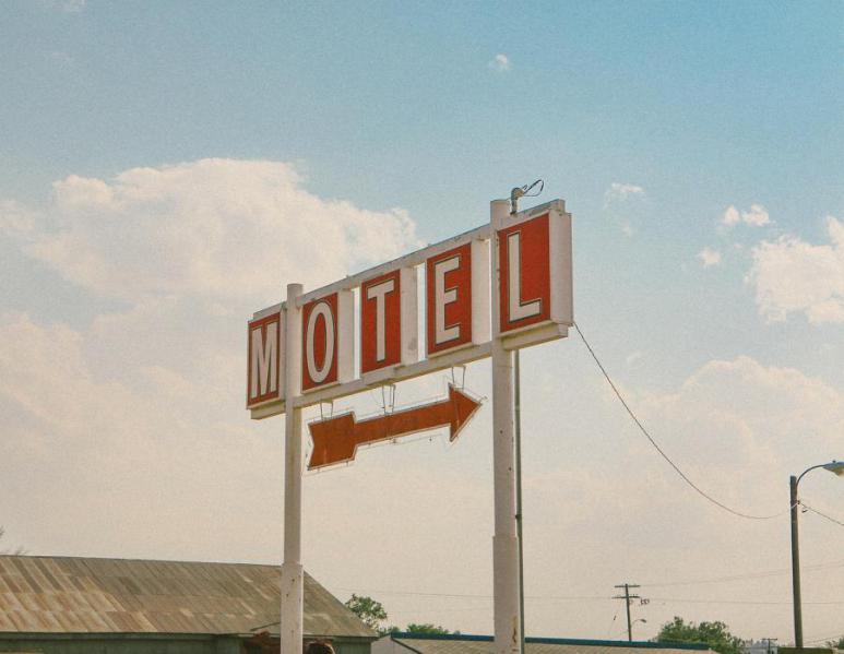 A motel sign with a red arrow pointing to the parking lot of the motel. The sign has five spaced out blocks with red backgrounds, each of which contains one letter spelling out MOTEL.