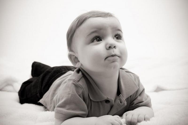 A black and white photo of a young child practicing "Tummy Time" by laying on their stomach. They are supporting their head on their own to look towards the top right of the frame.