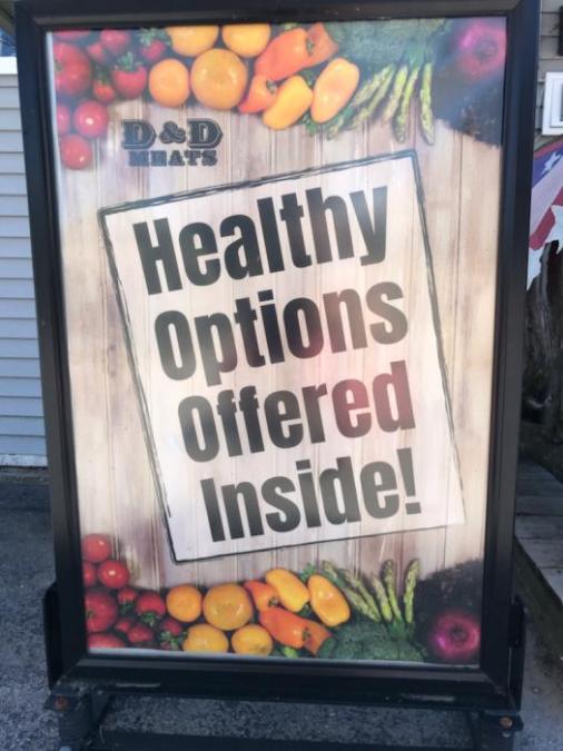 A sign is depicted saying "Healthy options offered inside!" The sign has fruits and colorful vegetables on the top and bottom of it.