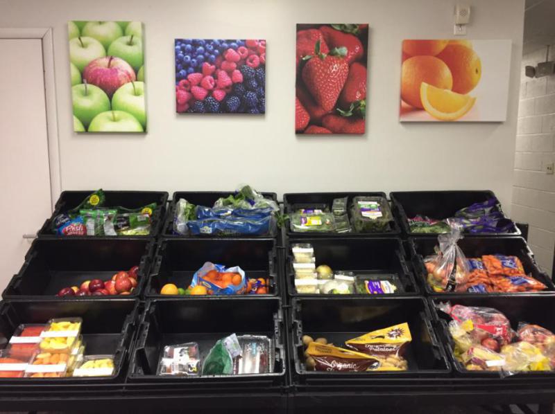 A stocked food pantry. There are black crates filled with many different kinds of food. The creates are placed in a 4 across, 3 down pattern. There are pictures of food above the creates  on the wall.